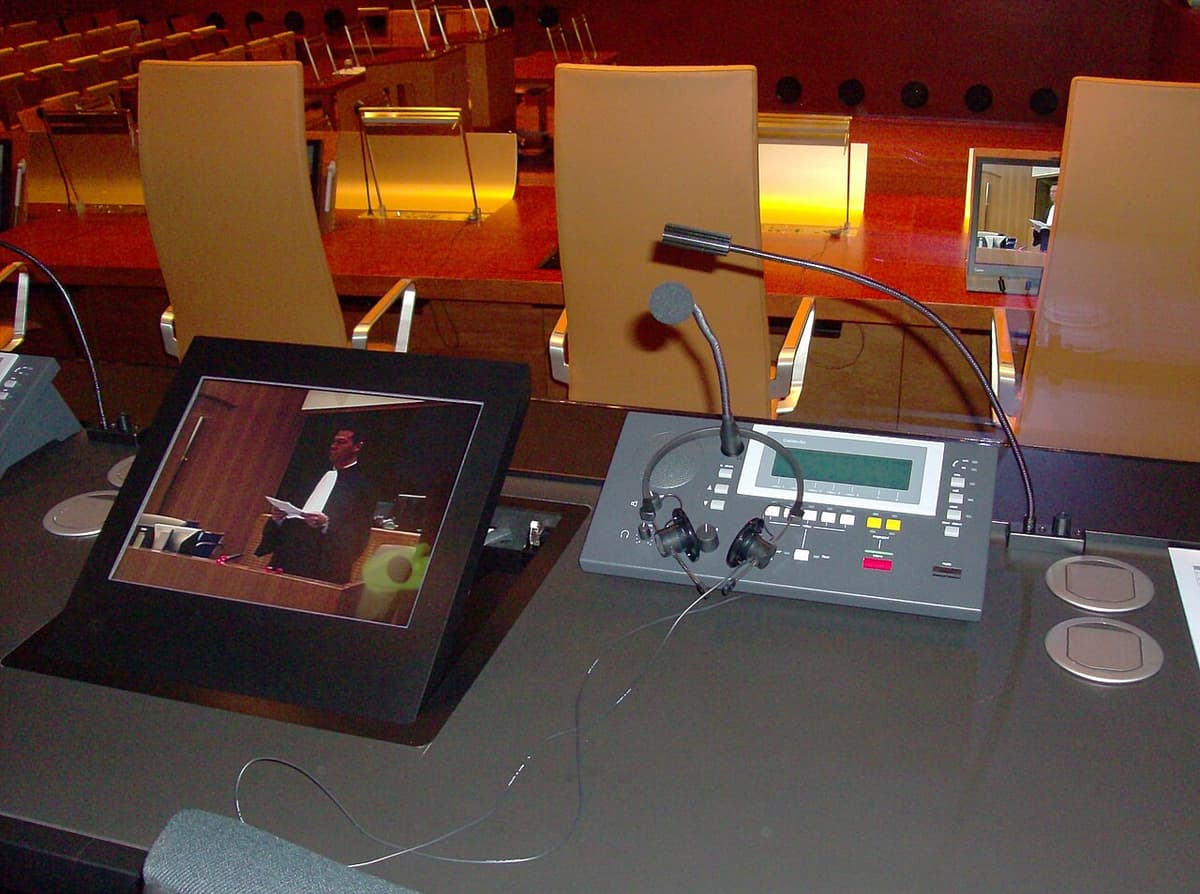 A simultaneous interpreter's workstation with headset, microphone and console overlooking a courtroom — the environment where shadowing became a training drill